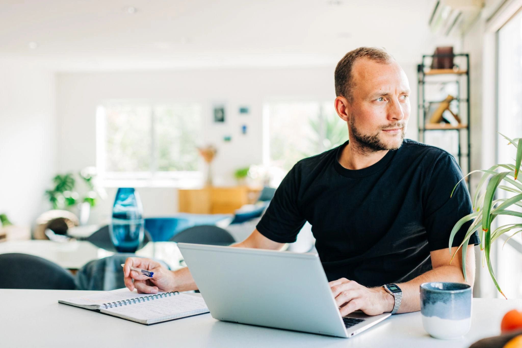Man working on a laptop, looking away thoughtfully.