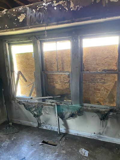 Burned room with damaged windows and boarded-up exterior.