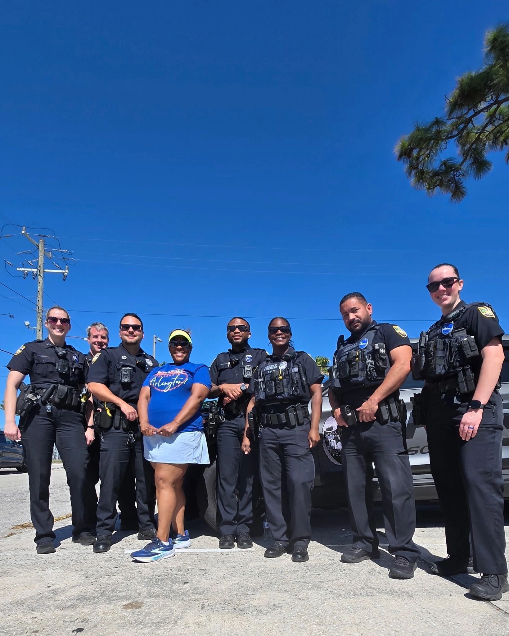 Group of police officers and a woman posing outside under clear blue sky.