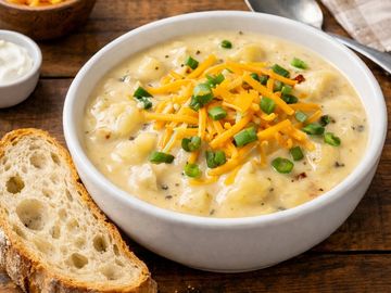 A bowl of creamy potato soup with cheese and green onions.