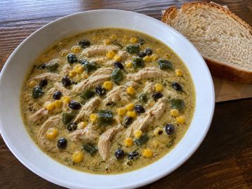 A bowl of chicken and vegetable soup with sliced bread.