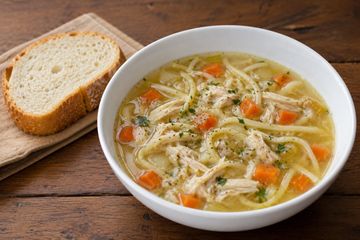 Bowl of chicken noodle soup with slice of bread.