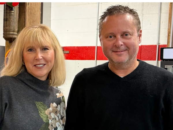A smiling man and woman posing indoors against a red and white wall.