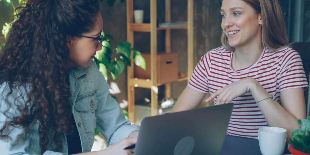Two women having a friendly discussion with a laptop and coffee.