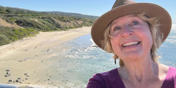 Smiling woman in a hat taking a selfie at a sunny beach.