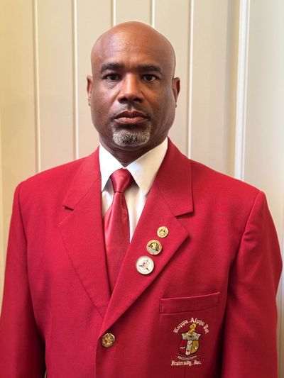 Man in a red blazer with fraternity pins and emblem.