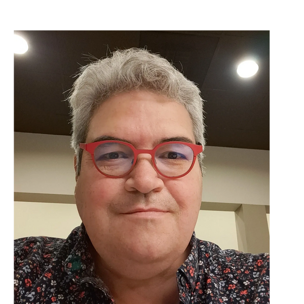 Man with gray hair and red glasses smiling indoors.