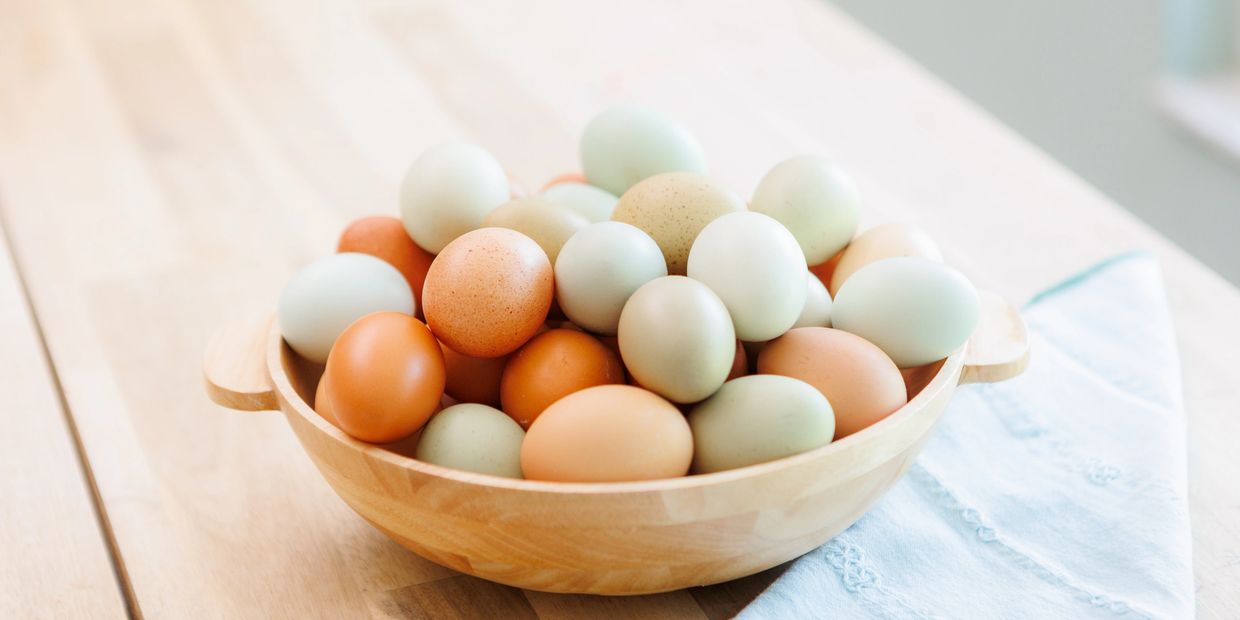 A wooden bowl filled with assorted colored eggs on a wooden table.