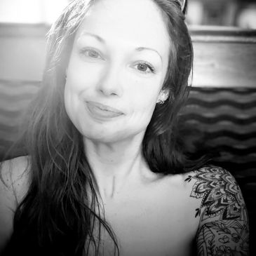 Black and white portrait of a woman with a detailed tattoo on her shoulder.