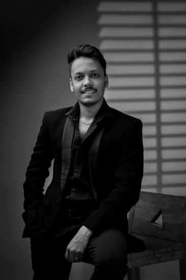 Young man in a black suit posing confidently.
