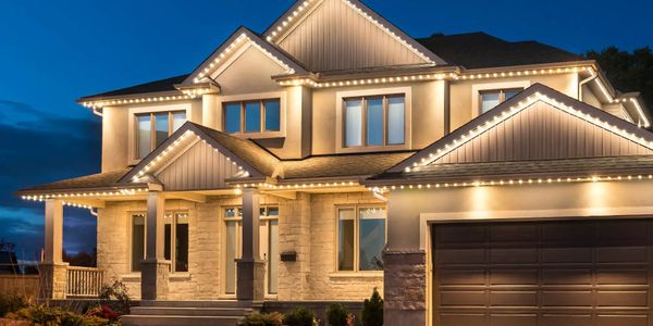 A modern two-story house illuminated with warm exterior lights at dusk.