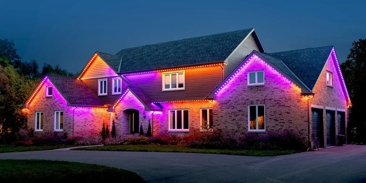 Modern brick house illuminated with vibrant purple and orange LED lights at dusk.