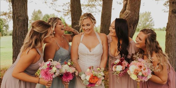 Bride and bridesmaids with bouquets standing in front of trees