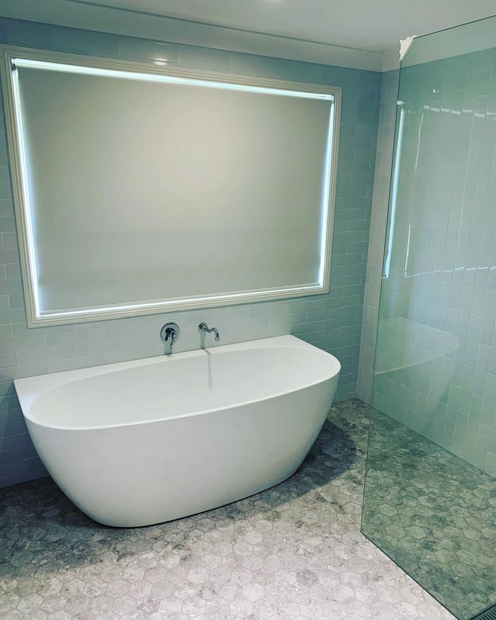 A freestanding bath with one straight side, mixer tap with spout and a mosaic floor.