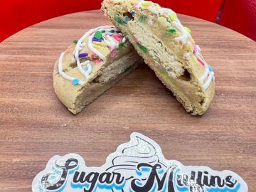 Colorful sprinkled sugar cookie cut in half on a wooden table.