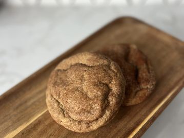 Two cinnamon sugar cookies on a wooden tray.
