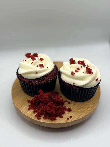 Two red velvet cupcakes with cream cheese frosting on a wooden plate.