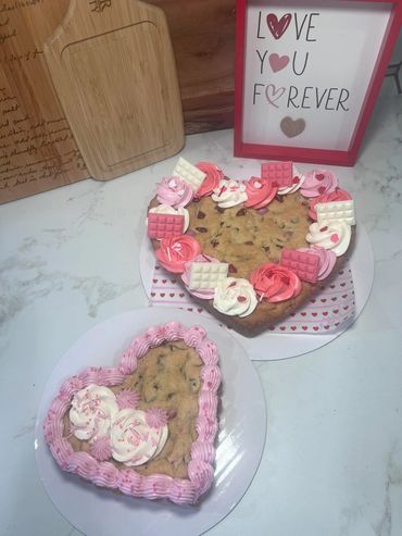 Two heart-shaped cookies decorated with pink and white frosting and chocolate pieces.