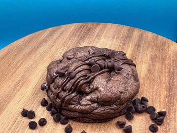 A large chocolate cookie with chocolate chips on a wooden board.