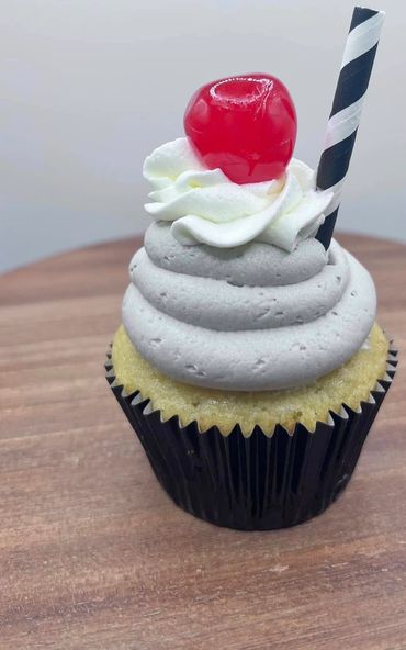 Vanilla cupcake with gray frosting, whipped cream, cherry, and striped straw.