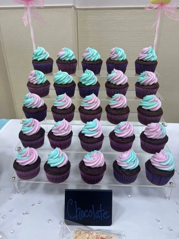 Chocolate cupcakes with pastel blue and pink swirled frosting arranged on a tiered stand.