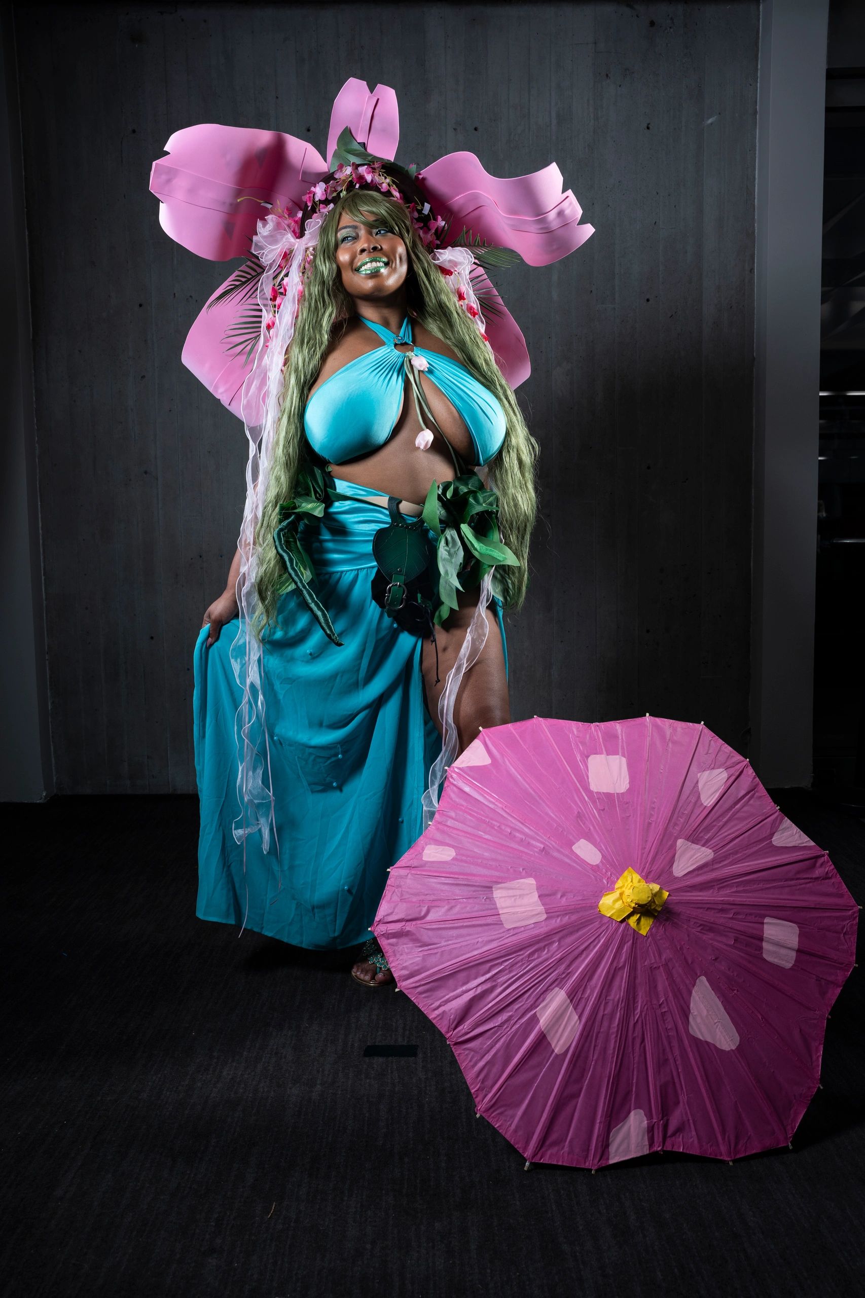 Person dressed in a vibrant floral-themed costume with pink umbrella.