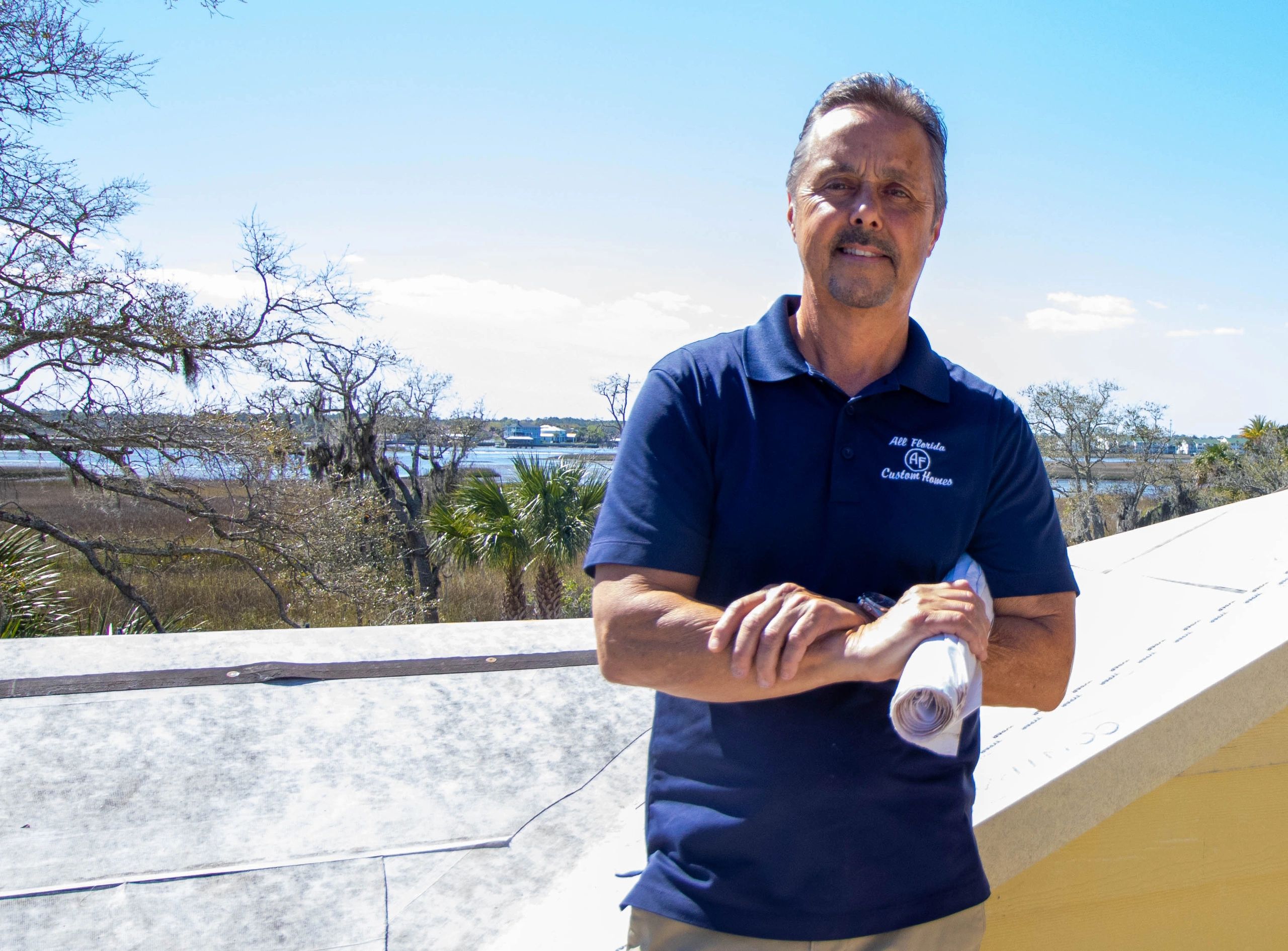 Man in navy polo shirt with rolled-up plans, outdoors.