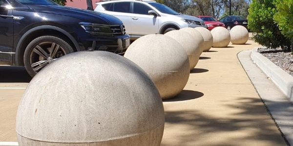 Concrete spherical bollards line a parking lot.