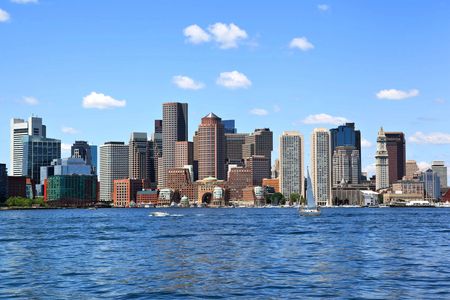 City skyline with tall buildings and water in the foreground on a sunny day.