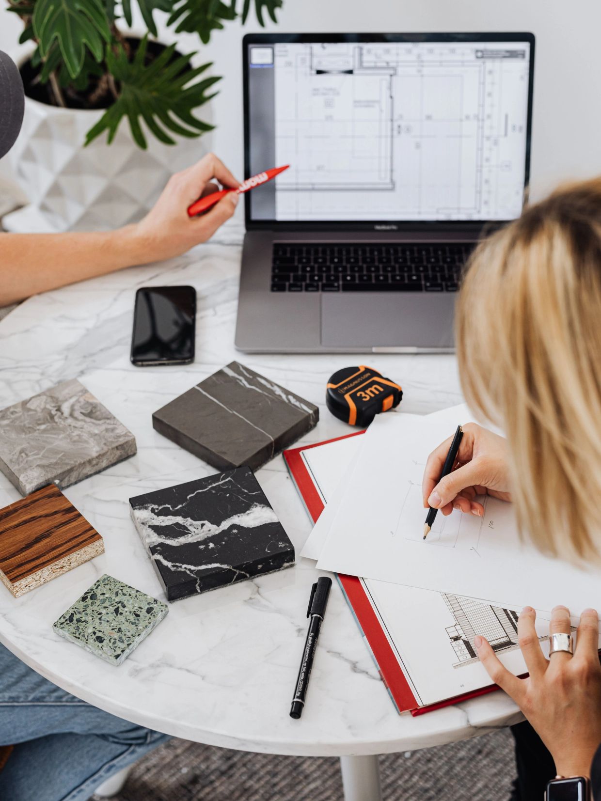 Two people reviewing architectural plans with material samples on table.
