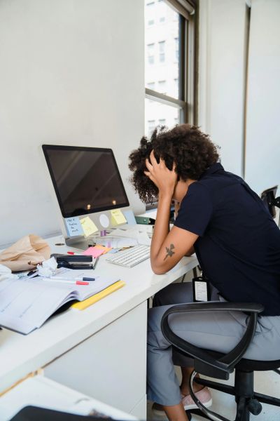 Person sitting at a cluttered desk, holding their head in frustration.