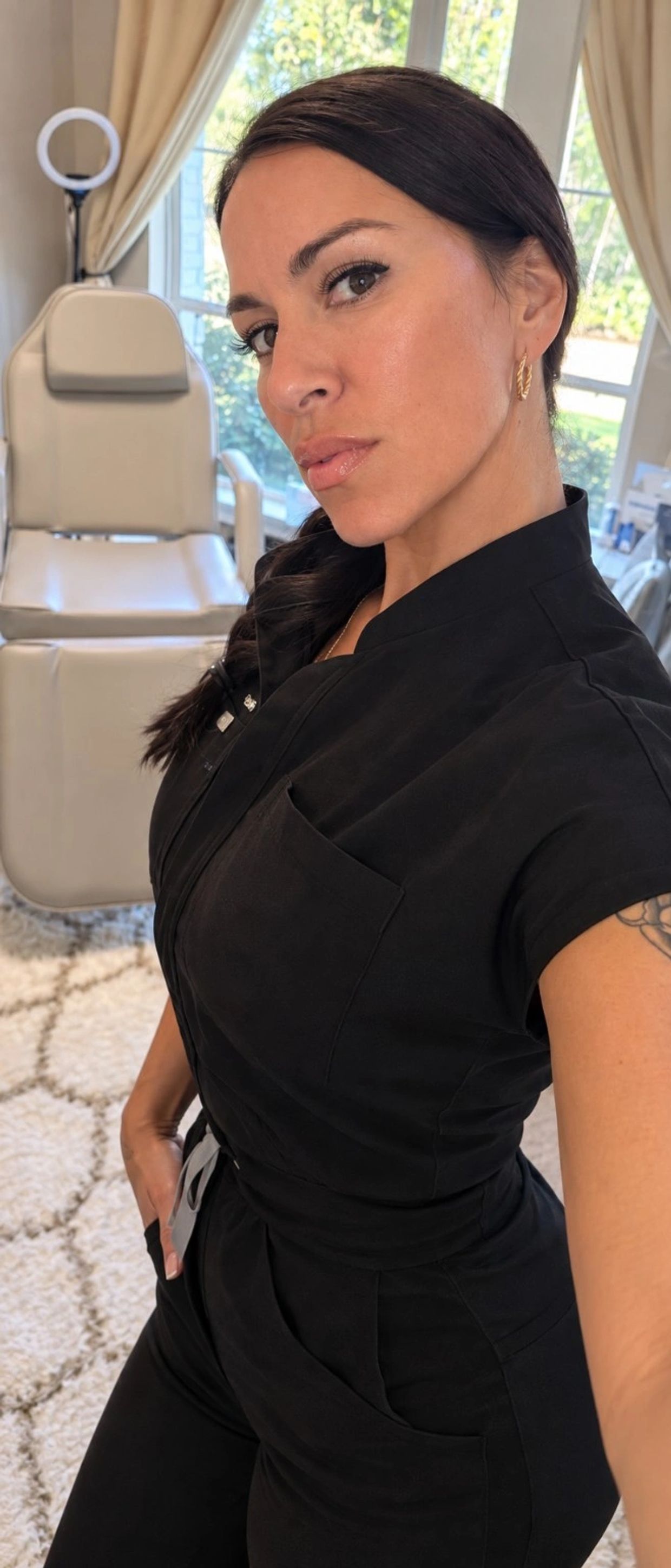 Woman in black scrubs takes a selfie in a bright room.