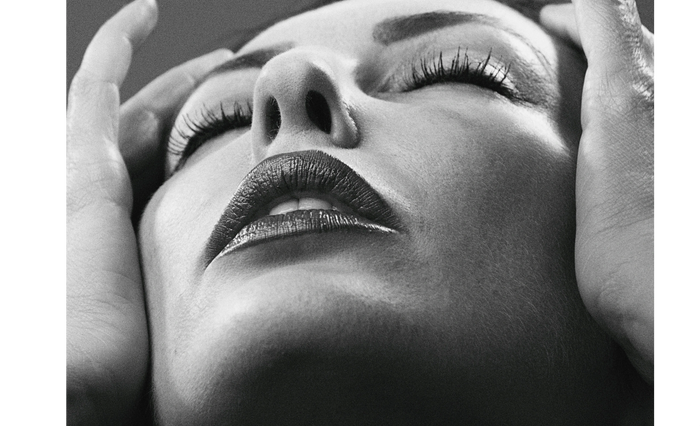 Close-up black and white portrait of a woman with closed eyes and hands touching her face.