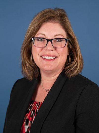 Smiling woman in glasses and business attire against a blue background.