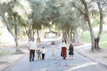Family of five holding hands and walking down a tree-lined path.