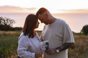 Couple sharing a tender moment at sunset by the sea with flowers.