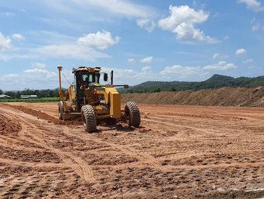 A grader machine leveling dirt on a construction site under a bright blue sky.