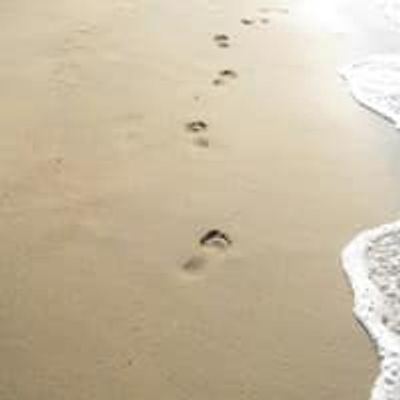 Footprints in the sand along the shoreline with gentle waves.