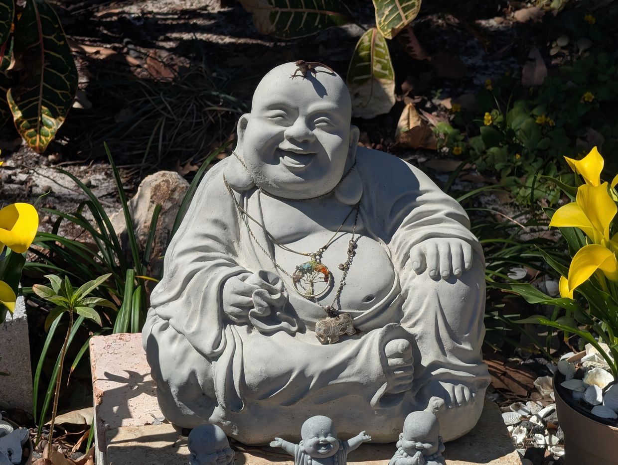 Laughing Buddha statue with lizard on head and yellow flowers.