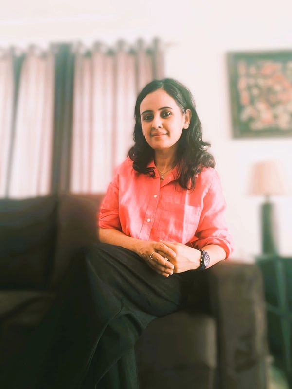 Woman sitting on a couch wearing a pink shirt and black skirt, smiling gently.