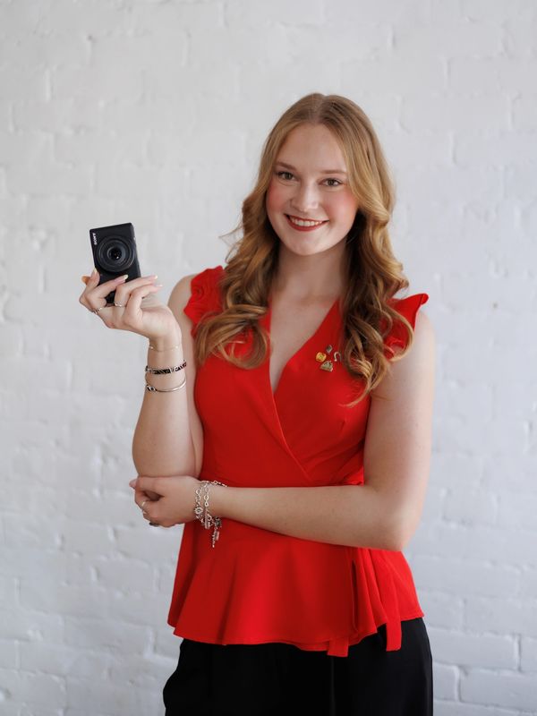Woman in red holding a camera and smiling.