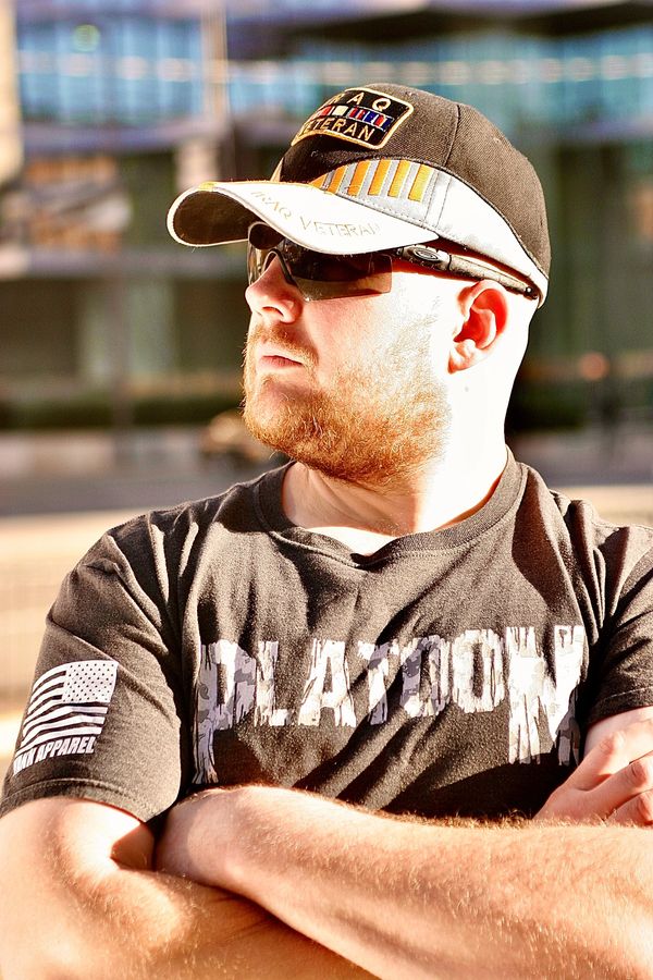 A guy wearing a hat and sunglasses with his arms crossed looking to his right