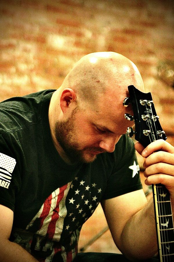 A guy sitting down praying with his guitar in his hand and against his head