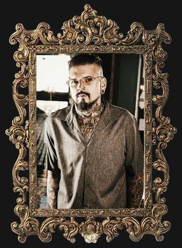 Man with tattoos and glasses in ornate frame.