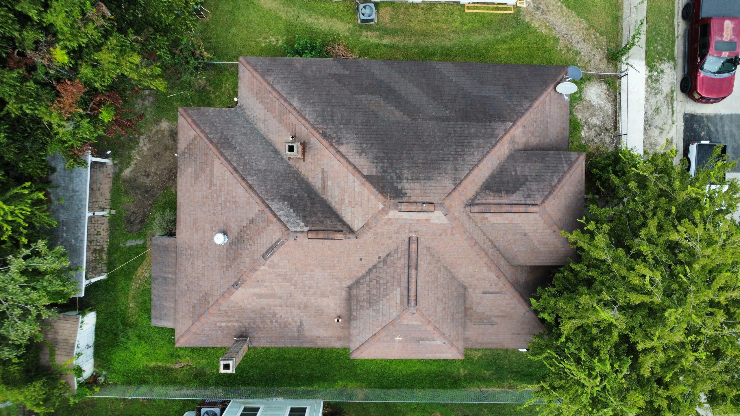 Aerial view of a house roof with a lawn and parked cars.