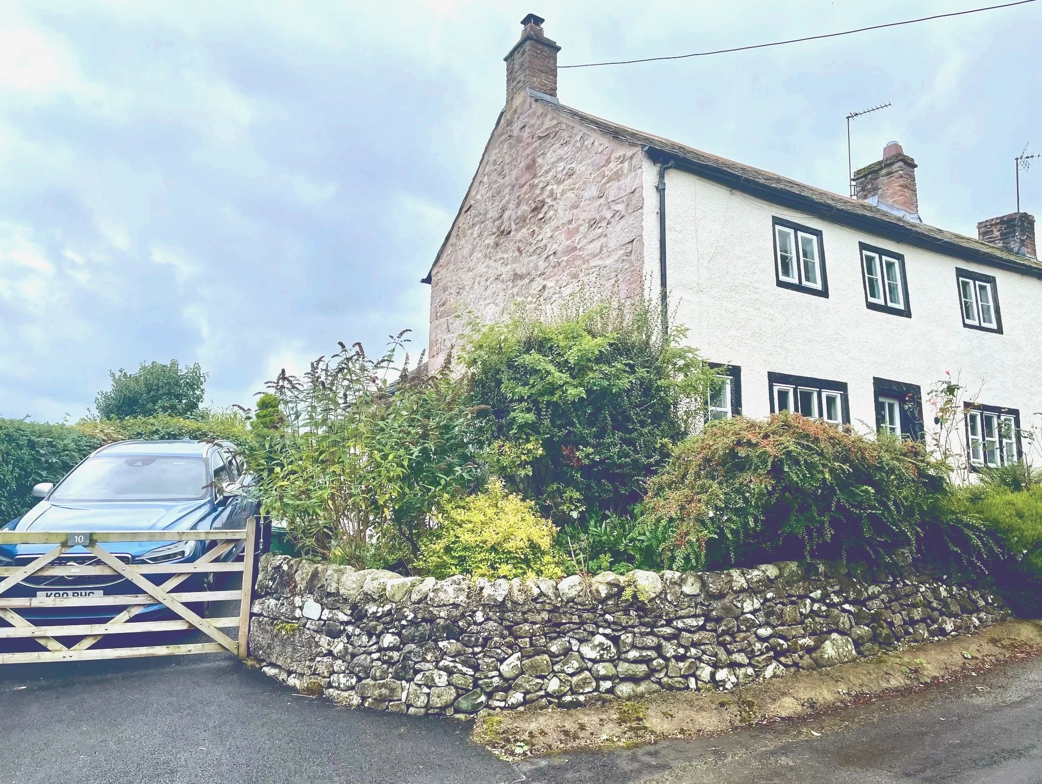 Stone cottage with black-trimmed windows and lush garden in front.