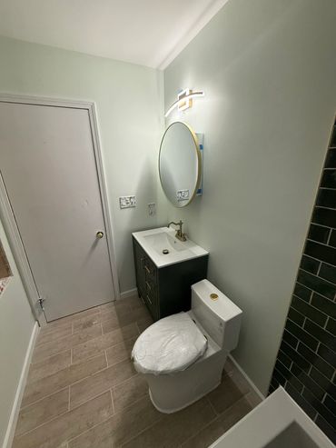 Modern bathroom with black vanity, white sink, round mirror, toilet, tiled floor, and green tile sho