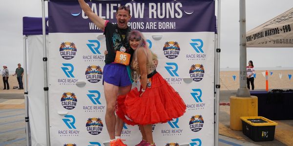 Two joyful runners celebrating on a podium at a Califlow Runs event by the beach.