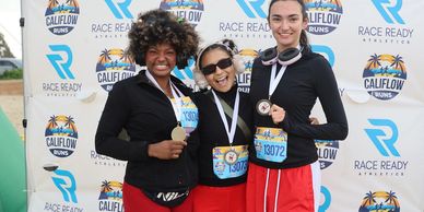 Three happy women showing medals at a race event.