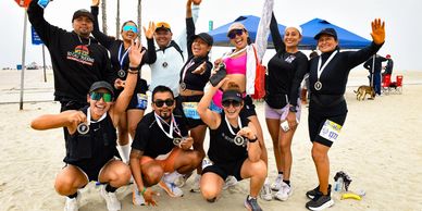 Group of runners celebrating on a beach with medals and smiles.